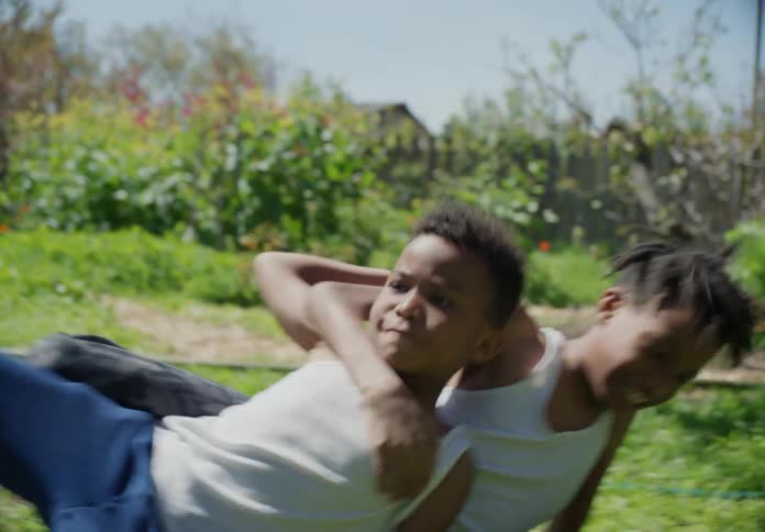 A pair of boys play fight in the yard of a house during the day