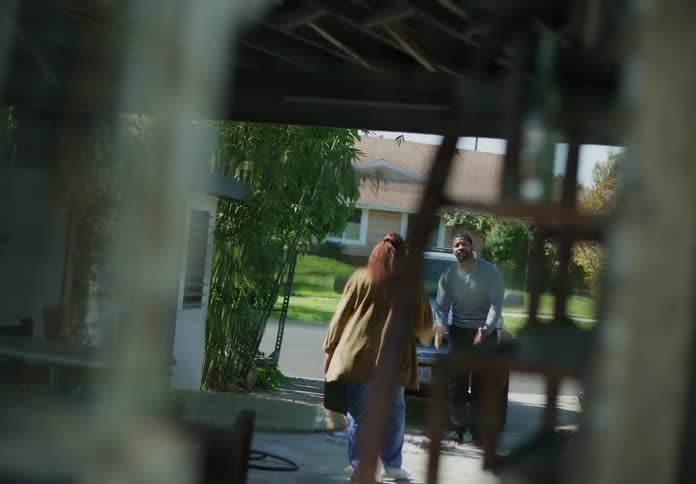 A man and woman standing in their driveway in front of a car arguing as the woman walks around