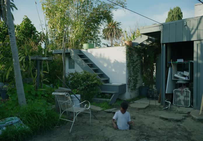 A boy plays in a dug up hole in his backyard