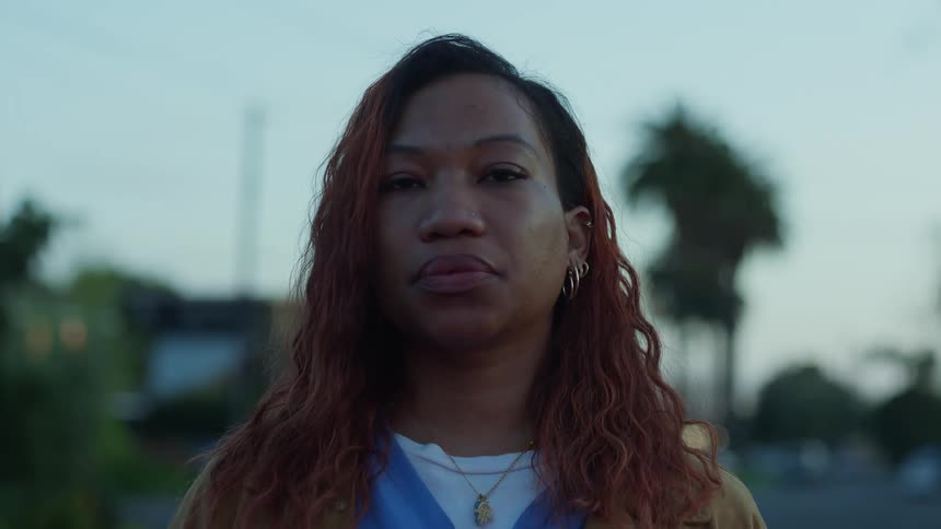 Woman with red curly hair earrings and necklace looks at camera in the street