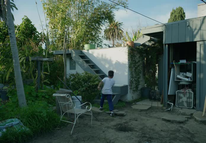 Boy comes out of a hole in the backyard ground and climbs the stairs on the side of the building