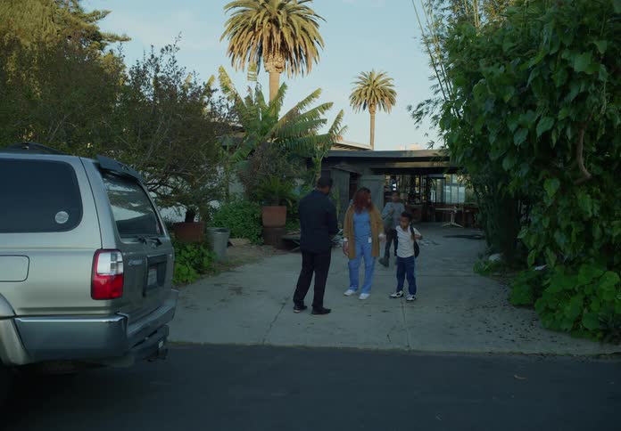 A man and woman chat in the driveway before the man takes his kids away in a car