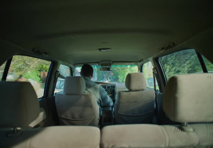 A man watches a woman walk away then backs out of the driveway and drives off