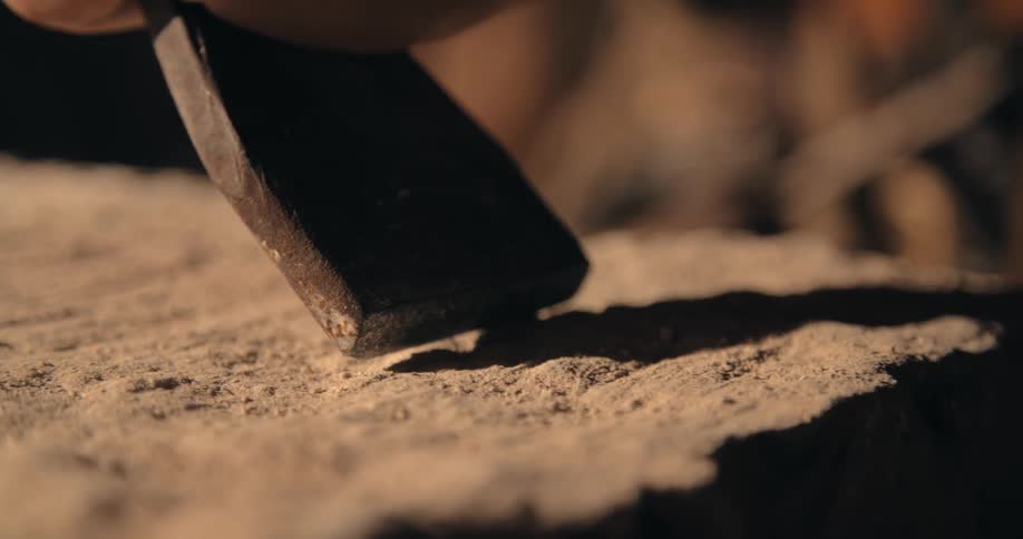 A close up of a stone working tool a person is hammering creating dust