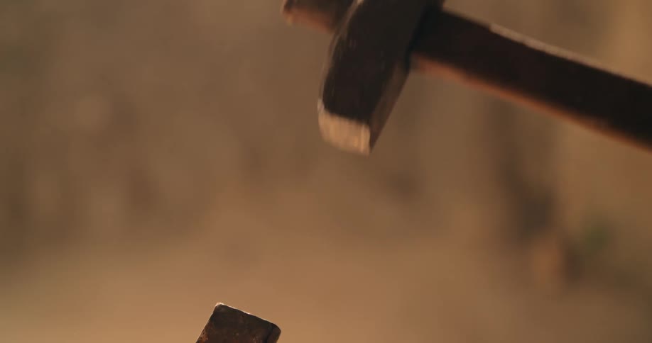 A simple hammer is swung downward and strikes a chisel