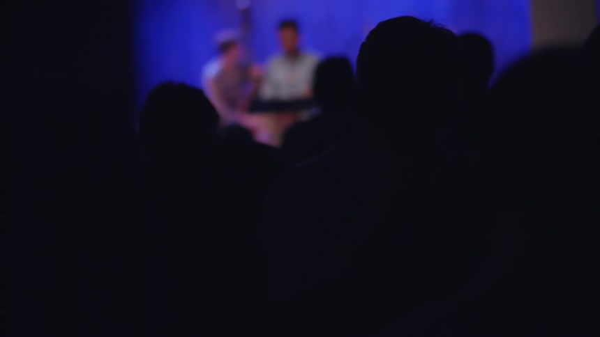 People performing on a lighted stage as seen through a crowd