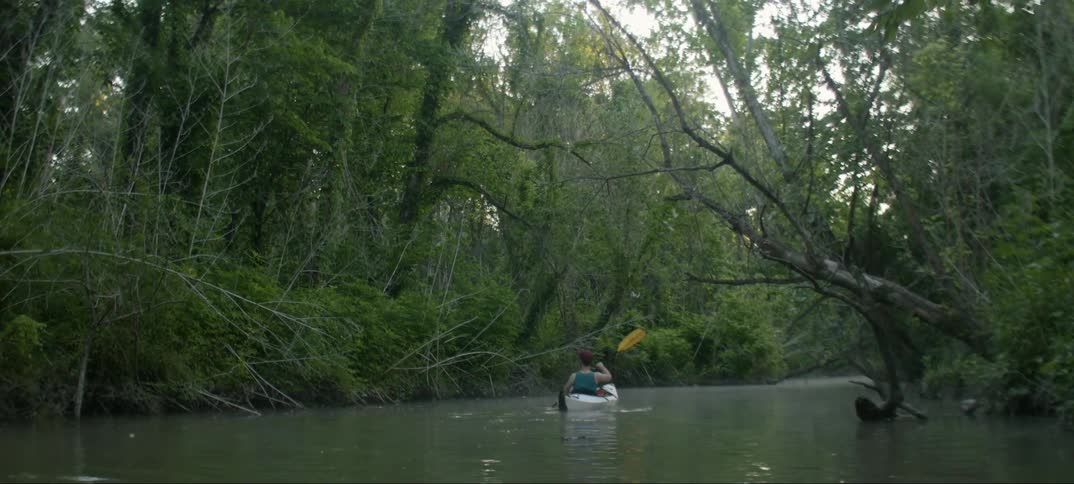A person paddles a kayak down a stream