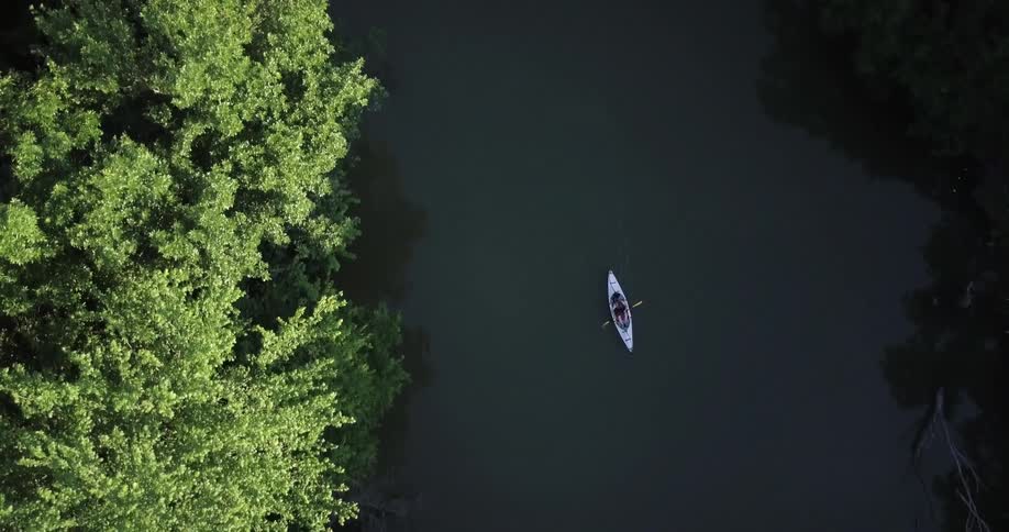 An overhead view of  someone paddling a canoe down a river surrounded by trees