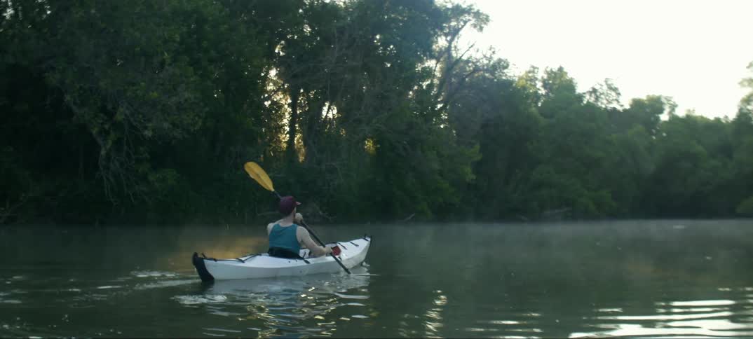A man kayaks on a river lined with trees