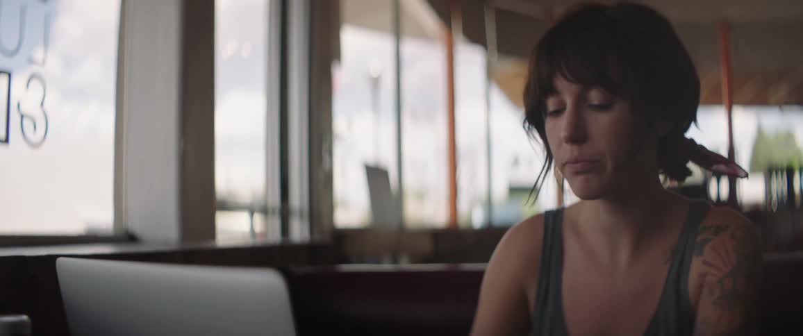 Woman sits in cafe in front of laptop and rubs her eyes