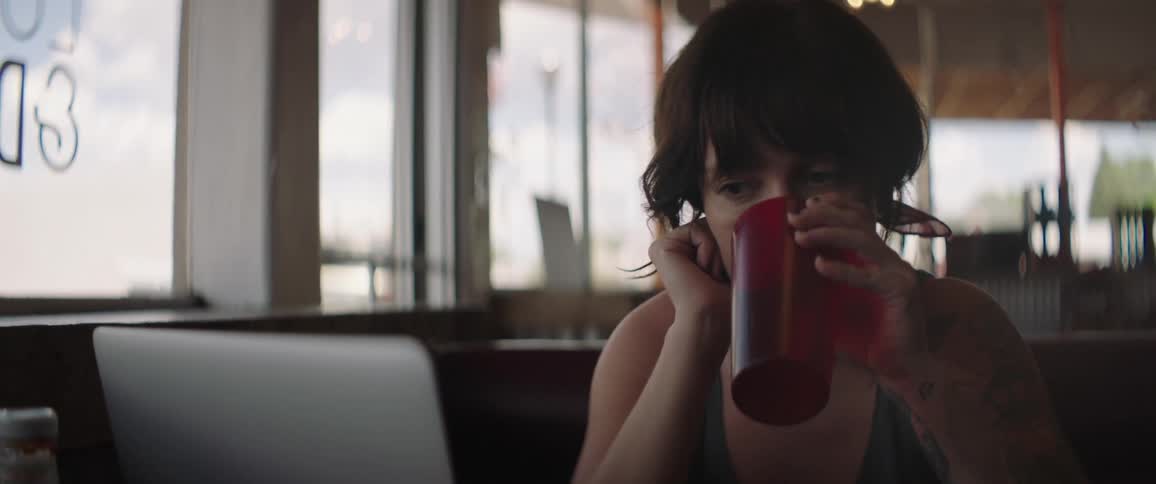 Woman sitting at the table drinks from red cup at a cafe