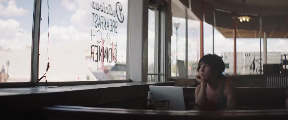 A woman sits alone in a restaurant booth while looking out of the window