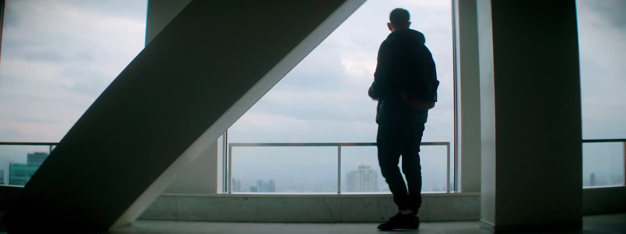 Man adjusts camera then walks toward window showing view of hazy city