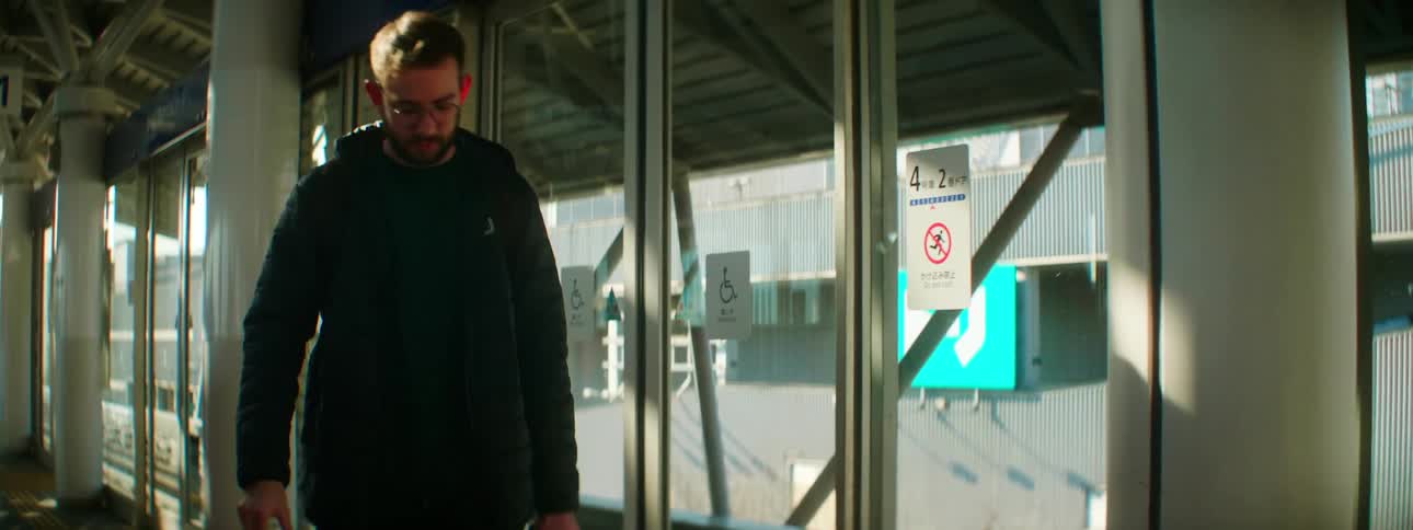 A man carrying a small camera walks next to a row of glass doors
