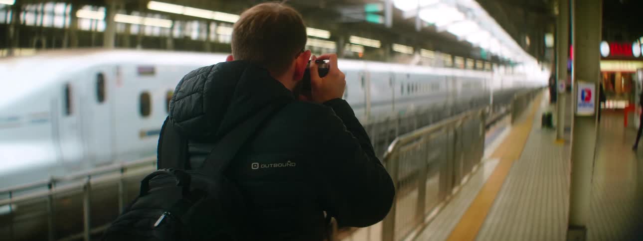 A photographer standing in a train station uses a camera to photograph a train as it pulls out of the station