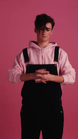 A young man rubbing and stretching his hands before crossing his arms while standing in a pink studio