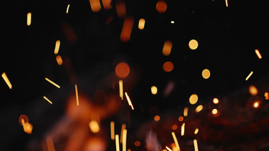 Sparks and embers from the fire rise in the darkness