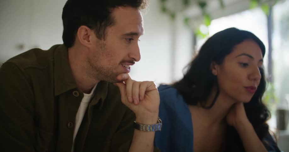 A man and woman talk with each other while looking at a laptop screen in the kitchen