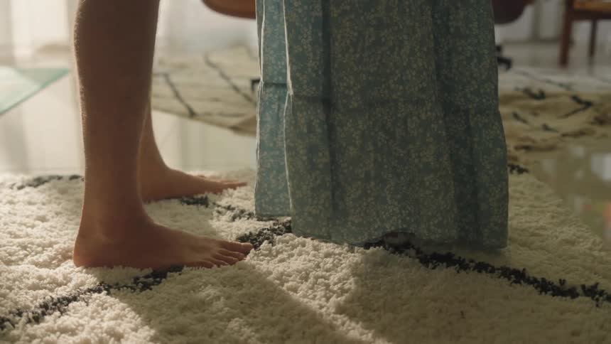 Close up of the bare feet of two women standing in front of each other over the rug in the living room
