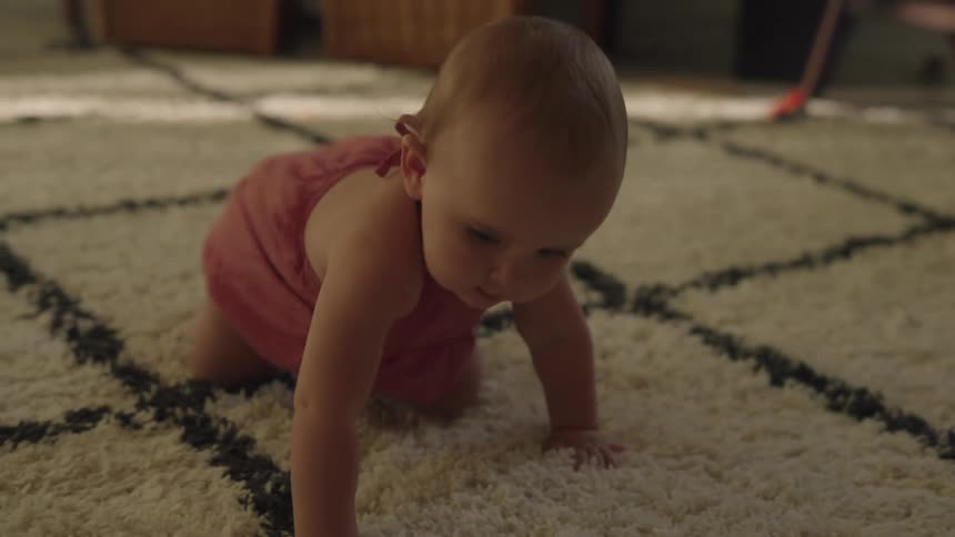A baby crawls around on a rug while her mom watches