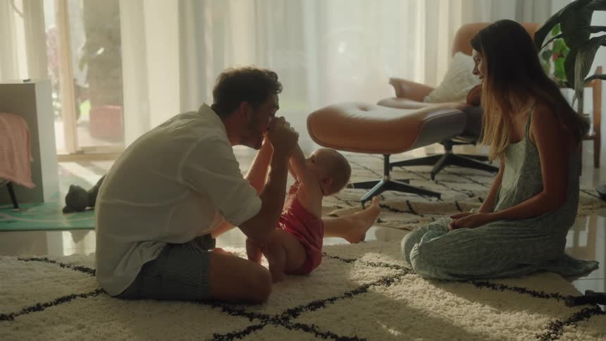 Mom and dad playing with baby at home on the floor standing her up laughing