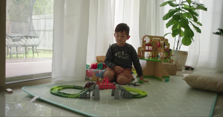 Boy sitting on the living room floor watching a toy car run on a track at daytime
