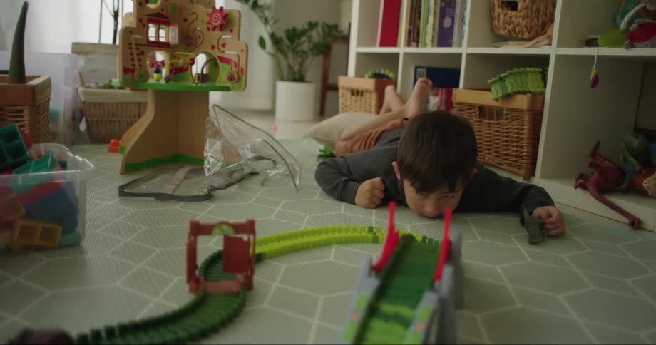 A little boy lays on his stomach and watches a toy car go around a race track