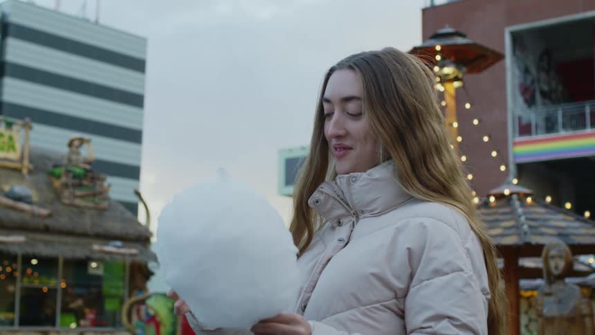 A woman standing outdoors while eating cotton candy and smiling