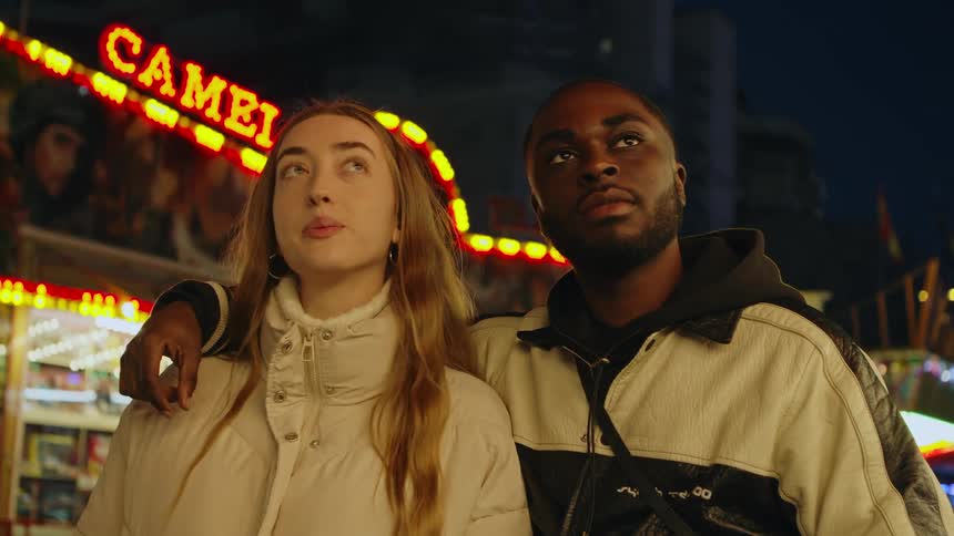 A man and woman stand together while taking in the sights at a carnival