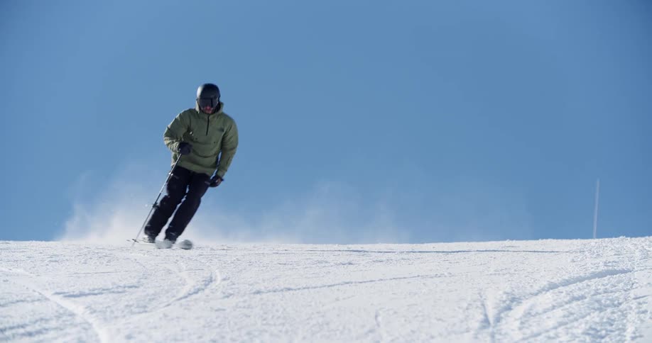 A skier holds their poles and zigzags down the snow covered slope