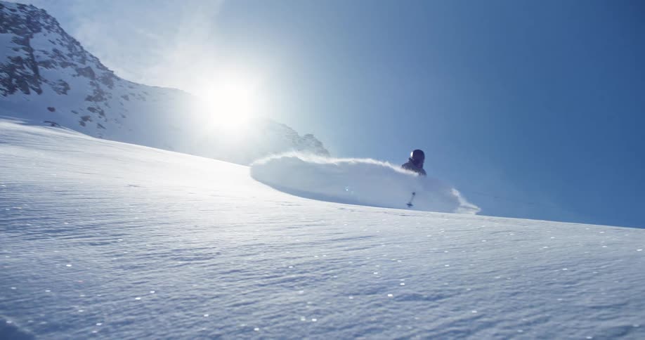 A skier sends snow spraying into the air behind them while descending a mountain slope