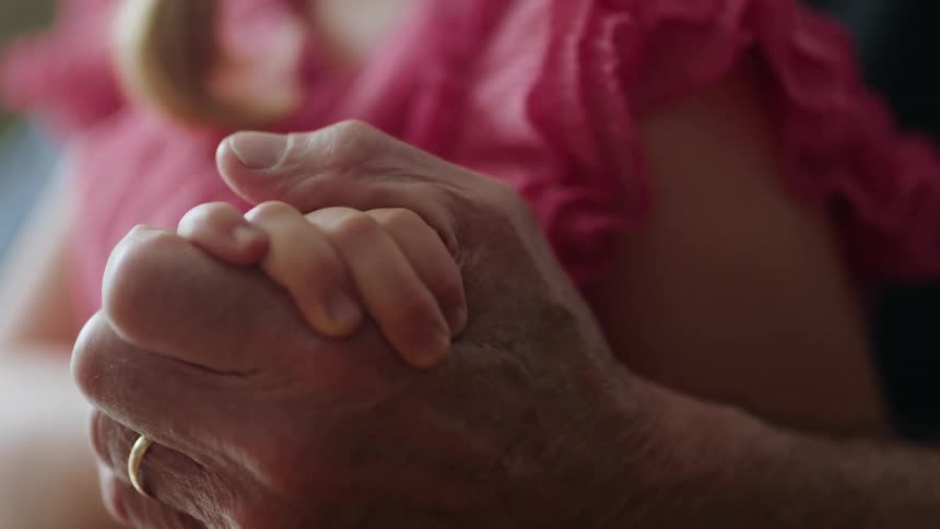 A young child squeezes the hand of an elderly person