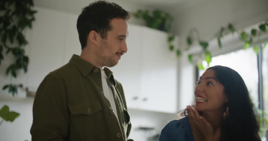 A man and woman standing at a kitchen counter while the woman is talking to the man smiling and laughing