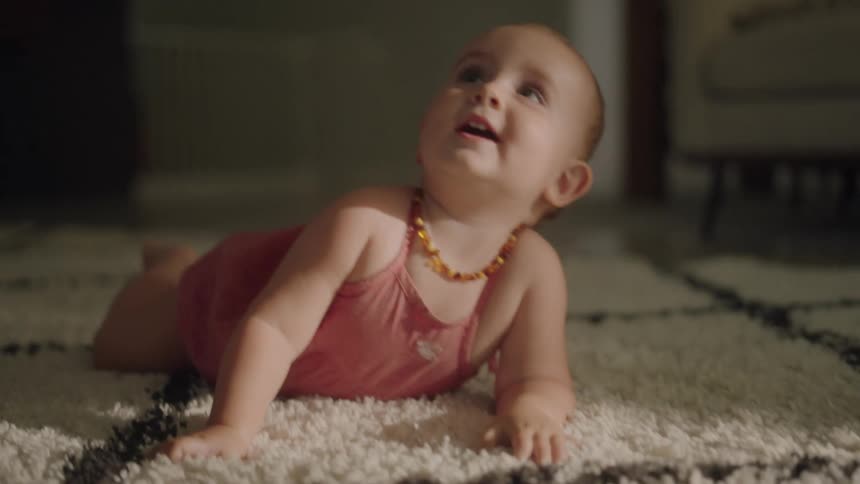 A baby girl crawls across a carpet before resting on her stomach