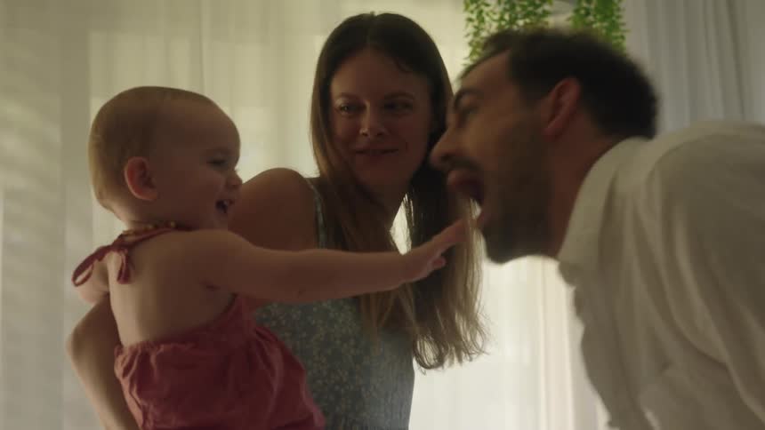 Father teasingly kisses hand of baby daughter held by her mother