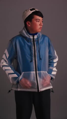 A man stands with his hands in the pockets of a sheer jacket as he turns his head modeling it