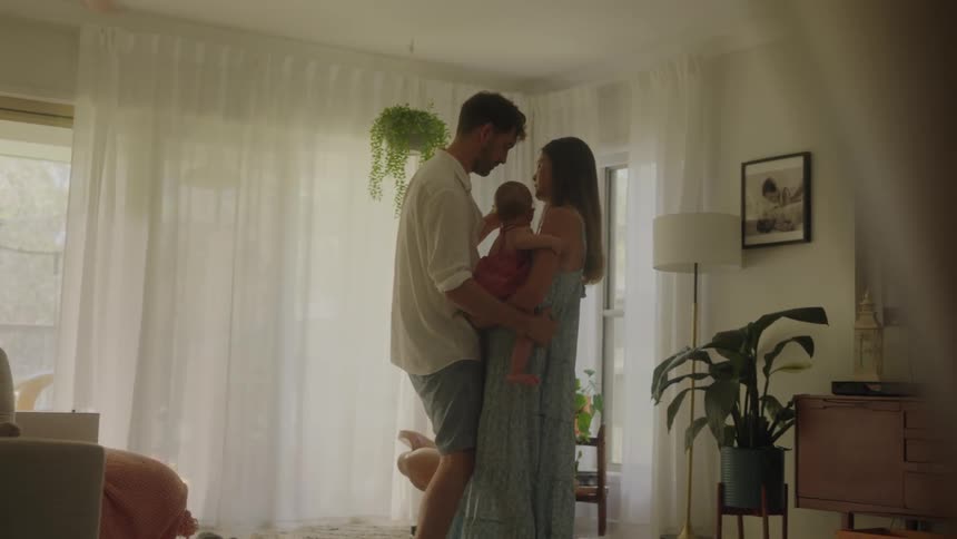 A couple slow dance with their baby in the living room