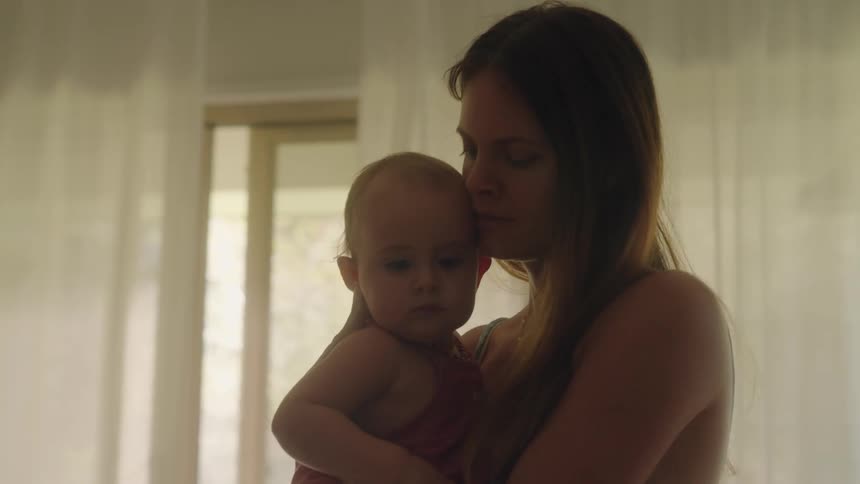 A woman rocks a baby in her arms while standing indoors during the day