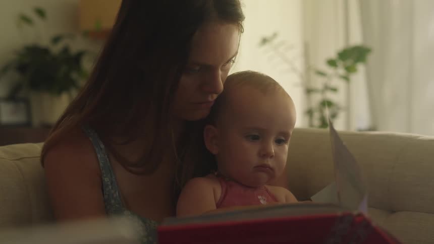 Mother reading a picture book to her baby sitting on her lap