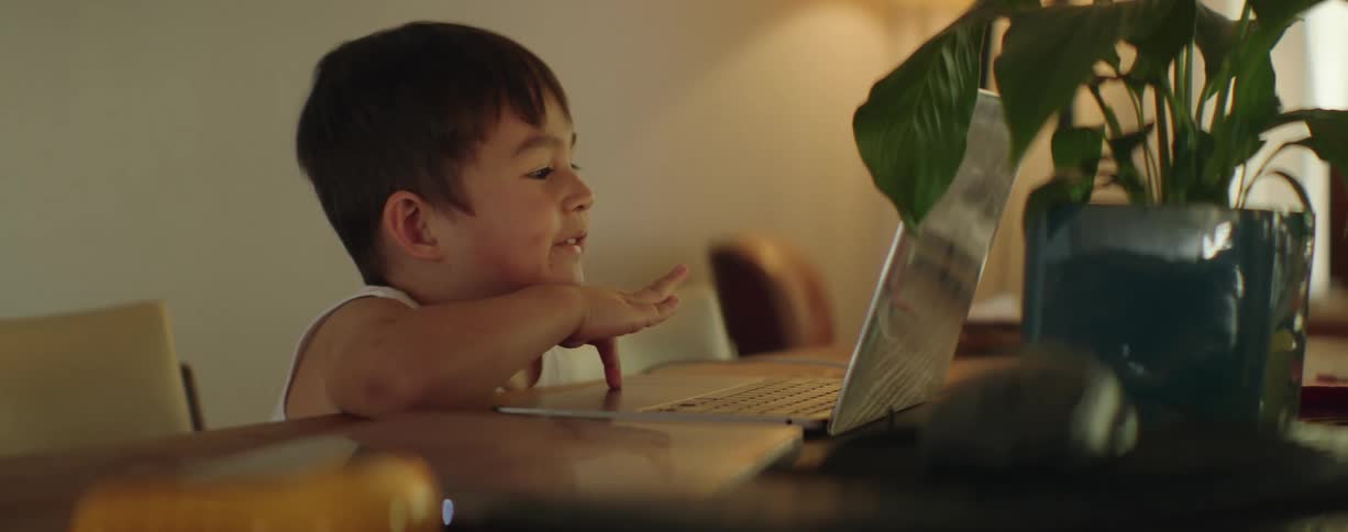 A little boy is sitting at a table typing on a laptop computer