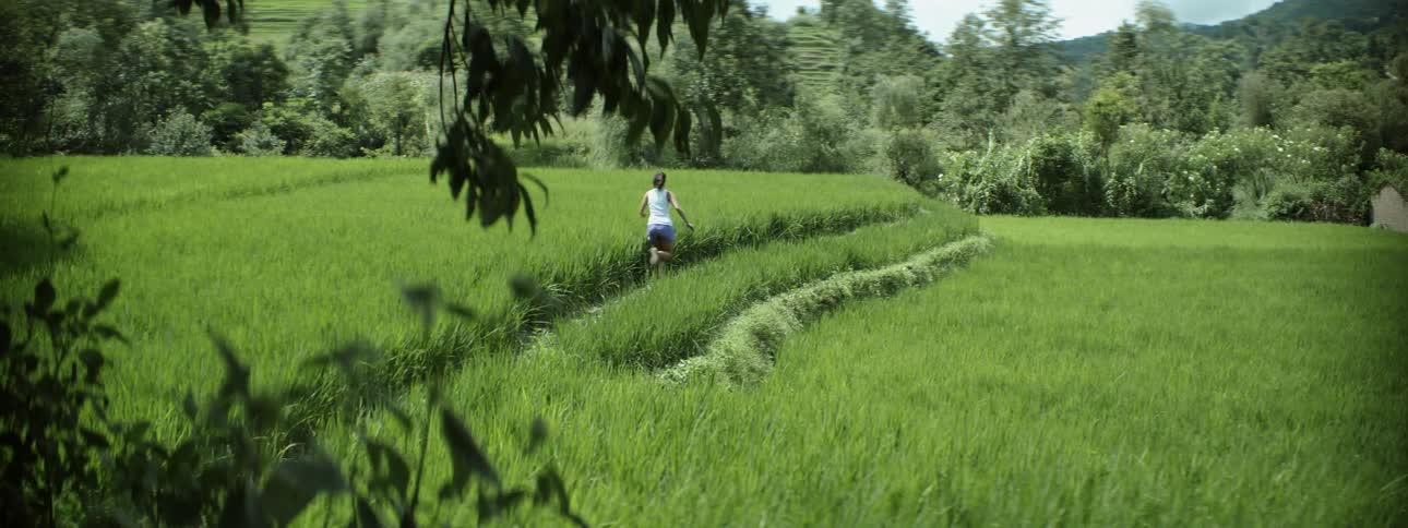 Determined woman with white shirt and purple shorts jogs in the green field