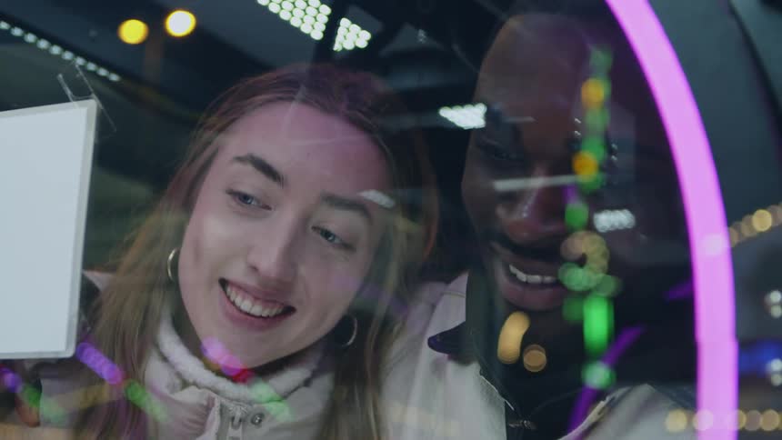 Close up of a young man and woman standing in front of an arcade game as they smile talk and laugh