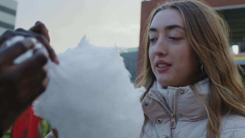 Young man and woman sharing cotton candy at a seasonal carnival at sundown