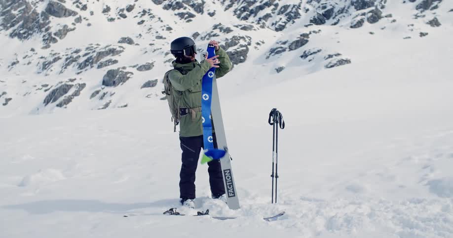 A skier attaching a sticker to his ski while standing in the snow