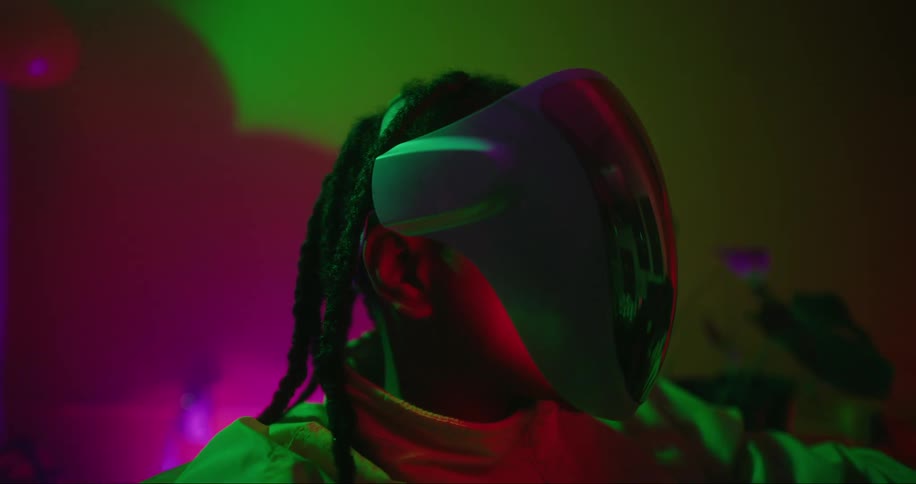 Close up of the head of a person with dreadlocks wearing a futuristic helmet inside a colorful room