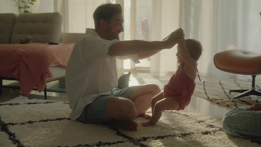 A man helps his infant daughter to stand up while the mother looks on