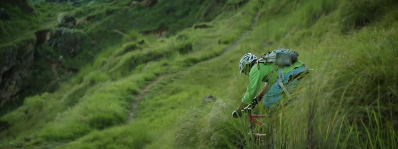 Two men ride bicycles through a grassy canyon