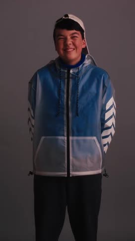 A teenager wearing a hat and a jacket bursts into laughter