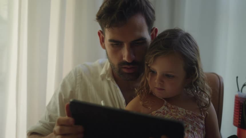 Father helps daughter write on tablet he holds while she sits in his lap