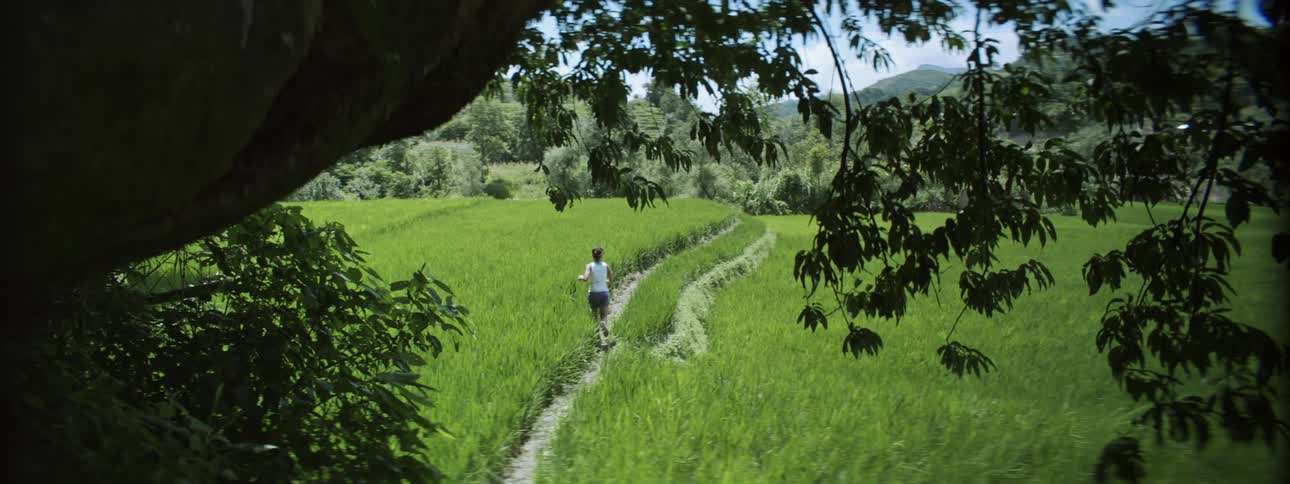 Young fit woman jogs on a path through a grass field in the countryside at daytime